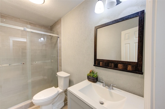 bathroom featuring a shower with door, vanity, a textured ceiling, and toilet