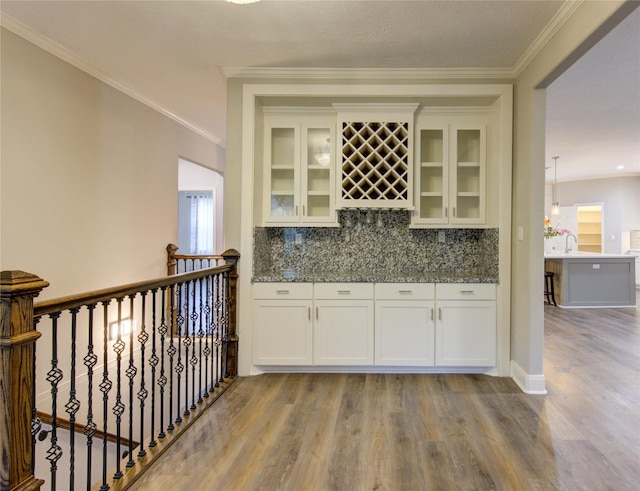 bar with light stone counters, white cabinetry, crown molding, and light wood-type flooring