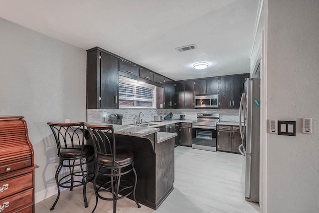 kitchen with a breakfast bar, sink, tasteful backsplash, kitchen peninsula, and stainless steel appliances