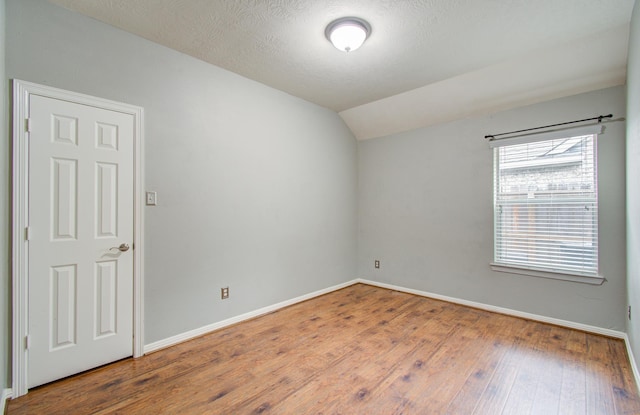 unfurnished room with hardwood / wood-style flooring, vaulted ceiling, and a textured ceiling