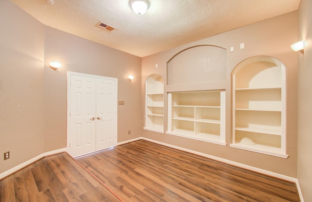 unfurnished room featuring hardwood / wood-style flooring, built in shelves, and a textured ceiling