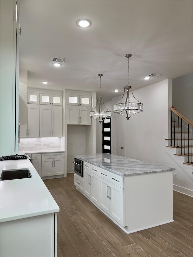 kitchen with hanging light fixtures, a kitchen island, dark wood-type flooring, and white cabinets