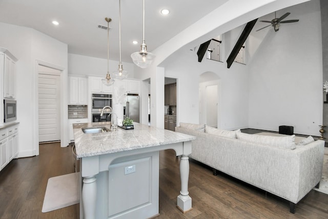 kitchen featuring appliances with stainless steel finishes, an island with sink, white cabinets, a kitchen bar, and decorative light fixtures