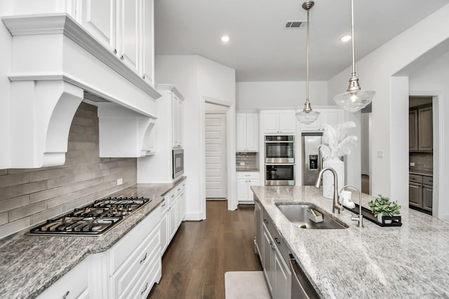 kitchen featuring sink, white cabinetry, hanging light fixtures, appliances with stainless steel finishes, and light stone countertops