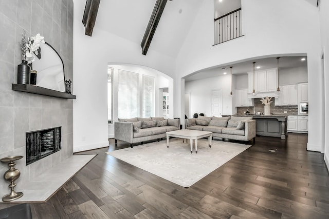 living room with a tiled fireplace, dark hardwood / wood-style floors, high vaulted ceiling, and beamed ceiling