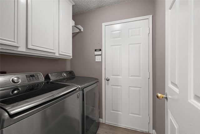 laundry area featuring cabinets, dark wood-type flooring, a textured ceiling, and washer and clothes dryer