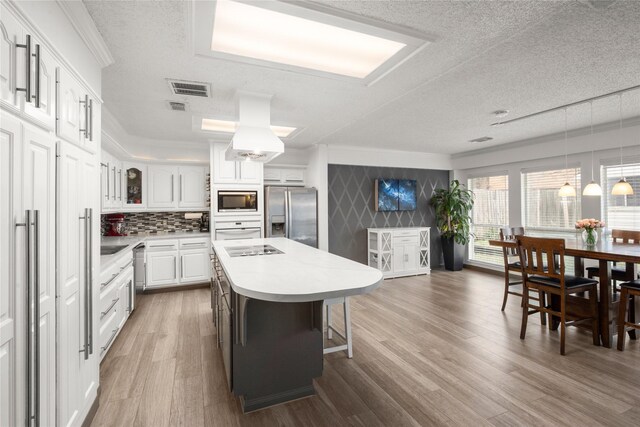 kitchen featuring hardwood / wood-style flooring, appliances with stainless steel finishes, a kitchen island, pendant lighting, and white cabinets