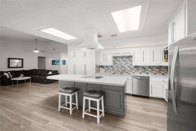 kitchen with a kitchen island, island range hood, white cabinetry, a kitchen bar, and stainless steel appliances