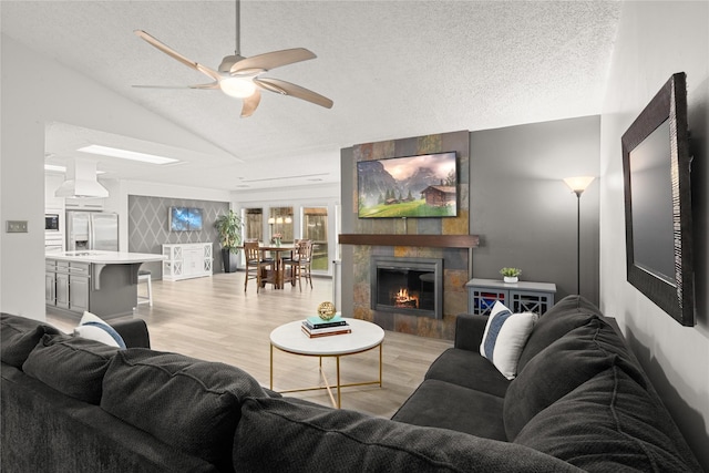 living room with a large fireplace, vaulted ceiling, light hardwood / wood-style flooring, and a textured ceiling