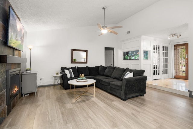 living room with high vaulted ceiling, a textured ceiling, a large fireplace, ceiling fan, and light hardwood / wood-style floors