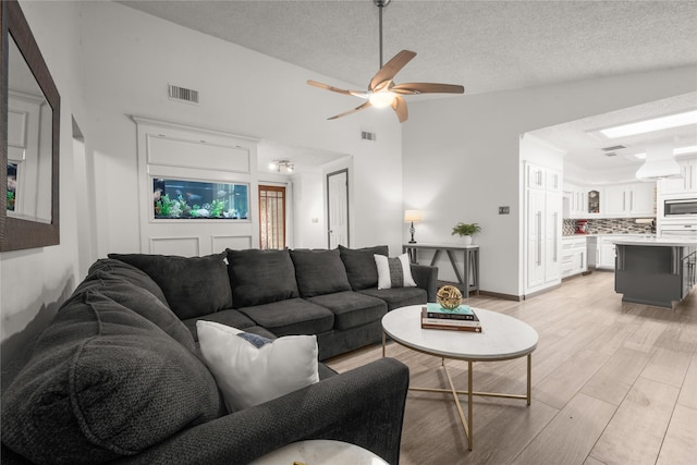 living room featuring ceiling fan, vaulted ceiling, a textured ceiling, and light wood-type flooring