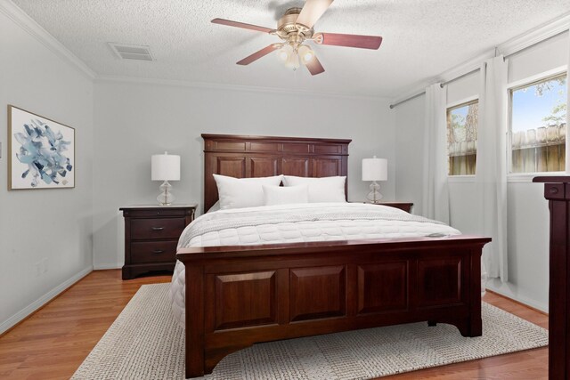 bedroom featuring ceiling fan, ornamental molding, a textured ceiling, and light wood-type flooring