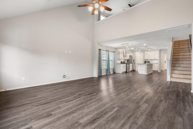 unfurnished living room with high vaulted ceiling, dark hardwood / wood-style floors, and ceiling fan with notable chandelier