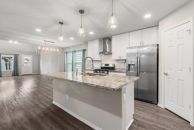 kitchen with a center island with sink, appliances with stainless steel finishes, decorative light fixtures, wall chimney range hood, and white cabinets