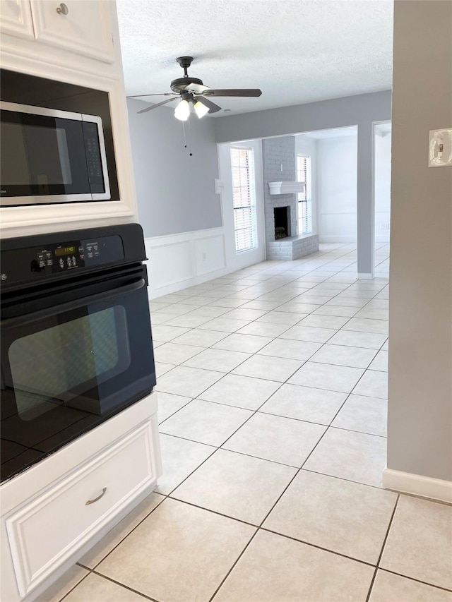 kitchen with white cabinetry, light tile patterned flooring, black oven, and a textured ceiling