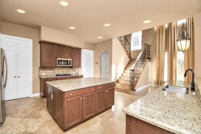 kitchen with sink, stainless steel appliances, light stone counters, tasteful backsplash, and a kitchen island