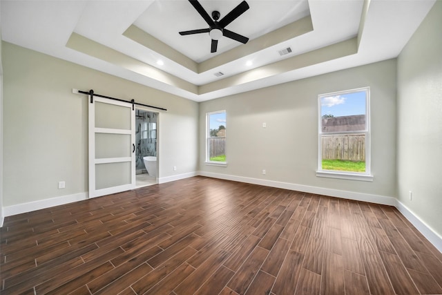 unfurnished room featuring a raised ceiling, a barn door, dark wood-type flooring, and plenty of natural light