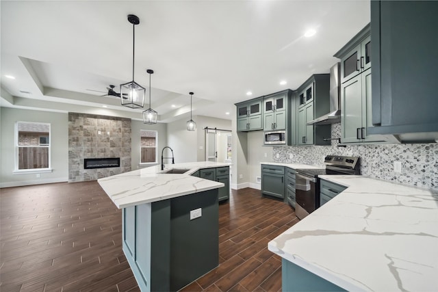 kitchen with pendant lighting, sink, stainless steel appliances, a barn door, and wall chimney exhaust hood