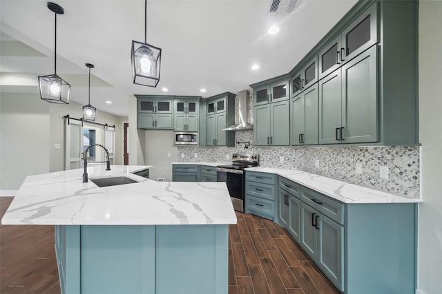 kitchen with decorative light fixtures, sink, stainless steel appliances, a barn door, and wall chimney exhaust hood