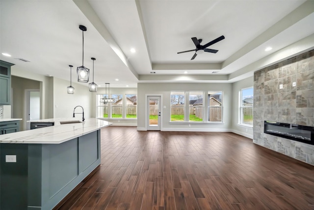 kitchen featuring sink, hanging light fixtures, a large island, light stone counters, and dark wood-type flooring