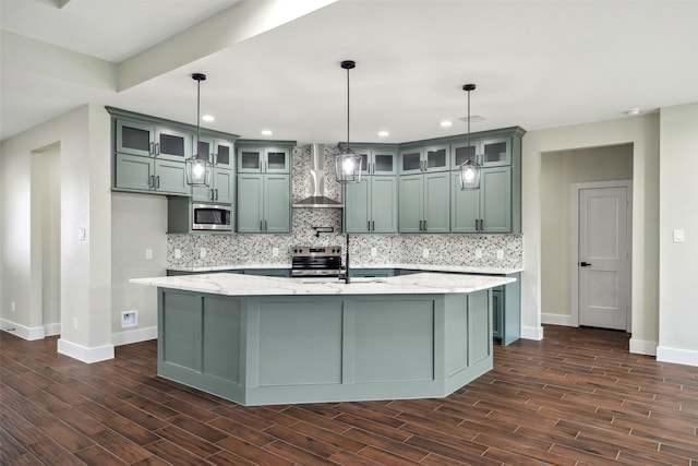 kitchen featuring light stone counters, wall chimney range hood, stainless steel appliances, and hanging light fixtures