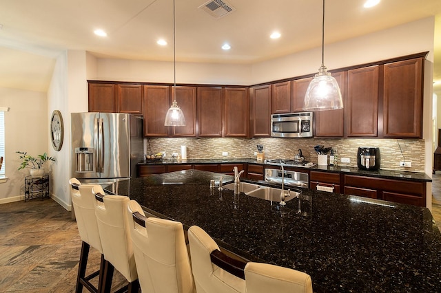 kitchen with dark stone countertops, appliances with stainless steel finishes, hanging light fixtures, and backsplash