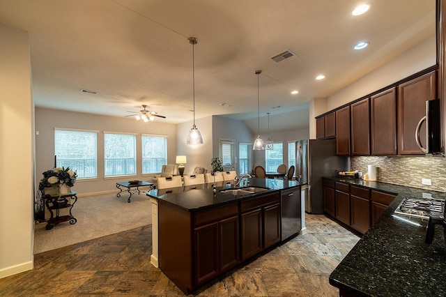 kitchen featuring sink, appliances with stainless steel finishes, hanging light fixtures, tasteful backsplash, and an island with sink