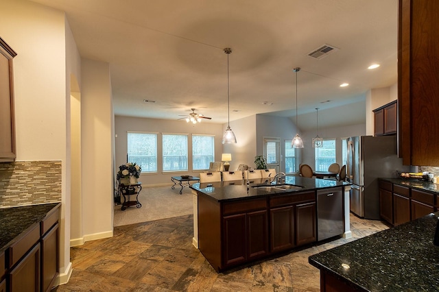 kitchen featuring sink, hanging light fixtures, stainless steel appliances, a center island with sink, and decorative backsplash