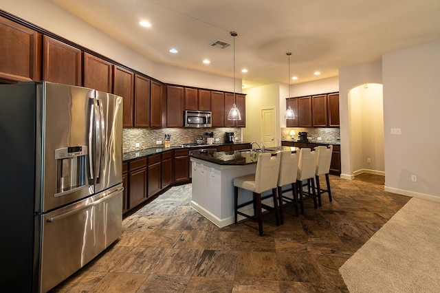 kitchen with backsplash, a kitchen bar, hanging light fixtures, a kitchen island with sink, and stainless steel appliances