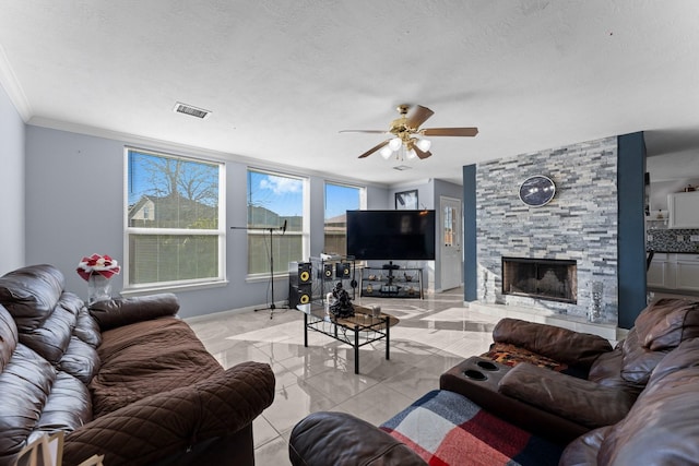 tiled living room with crown molding, ceiling fan, a stone fireplace, and a textured ceiling