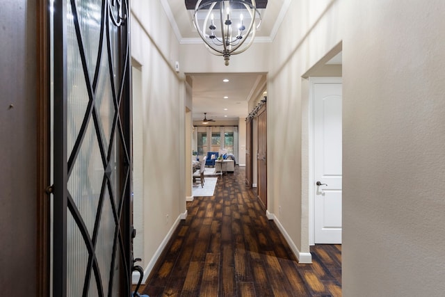 hallway with dark hardwood / wood-style flooring, a notable chandelier, crown molding, and a barn door