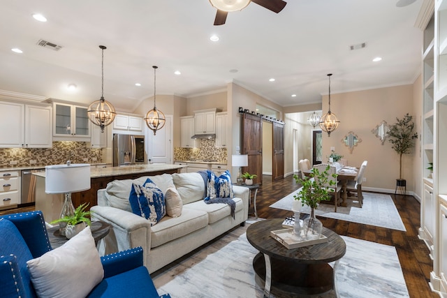 living room with ornamental molding, a barn door, dark hardwood / wood-style floors, and ceiling fan with notable chandelier