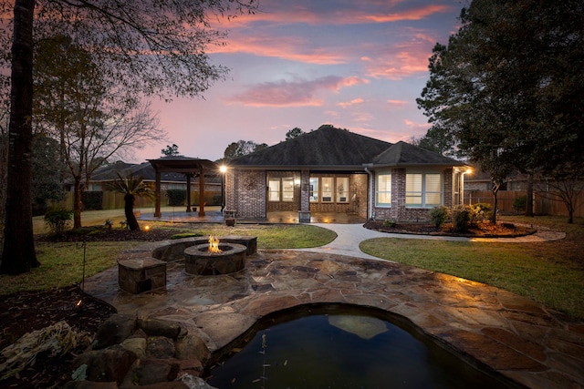 back house at dusk featuring a patio, a fire pit, and a lawn