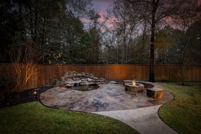 patio terrace at dusk featuring an outdoor fire pit and a lawn