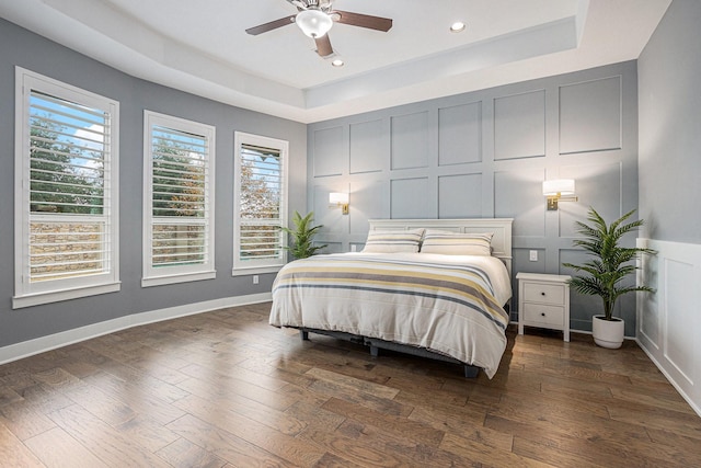 bedroom with a raised ceiling, multiple windows, and dark wood-type flooring