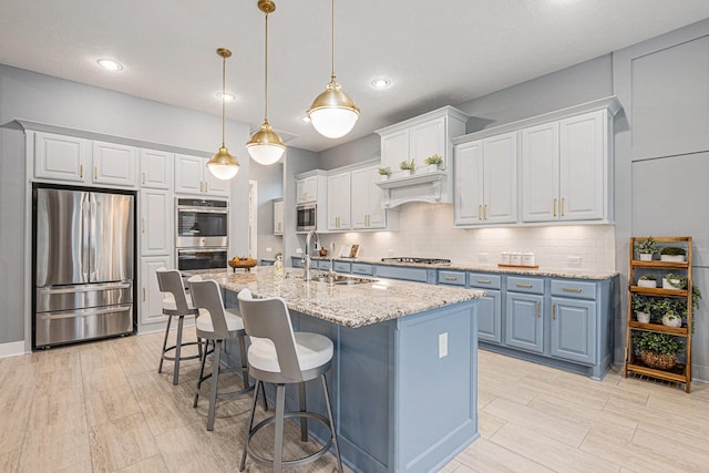 kitchen featuring a center island with sink, sink, white cabinetry, pendant lighting, and stainless steel appliances