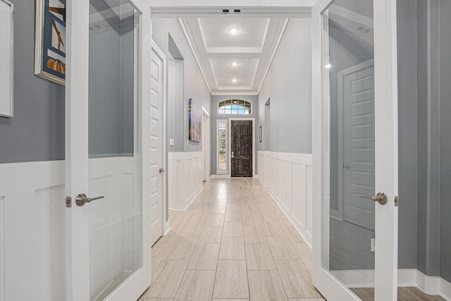 hallway featuring light wood-type flooring, crown molding, and a raised ceiling