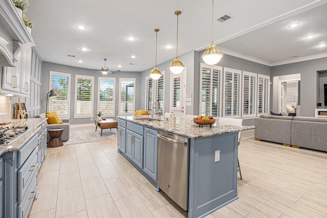 kitchen with appliances with stainless steel finishes, a center island with sink, light stone counters, decorative light fixtures, and sink