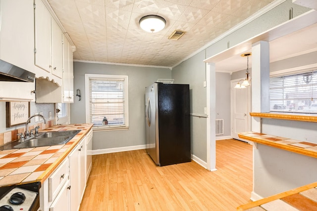 kitchen with sink, stainless steel refrigerator, hanging light fixtures, white cabinets, and tile countertops