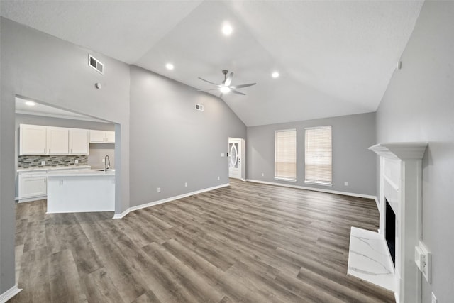 unfurnished living room featuring wood-type flooring, high vaulted ceiling, sink, and ceiling fan