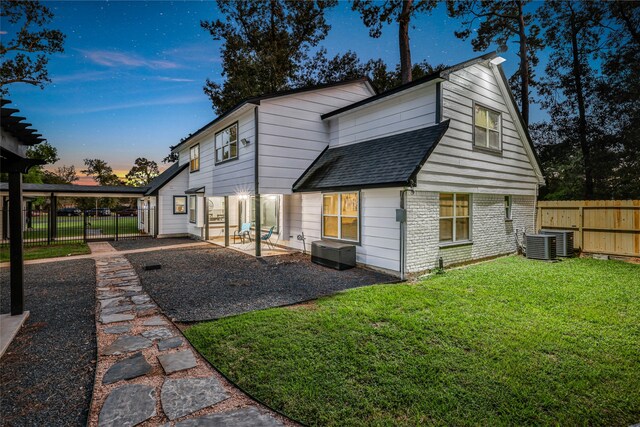 back house at dusk with a lawn, central air condition unit, and a patio area