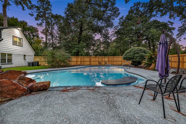 pool at dusk featuring cooling unit and a patio area