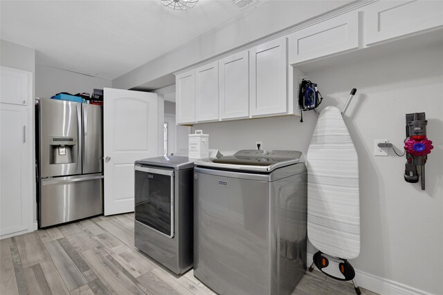 clothes washing area featuring independent washer and dryer, light hardwood / wood-style flooring, and cabinets