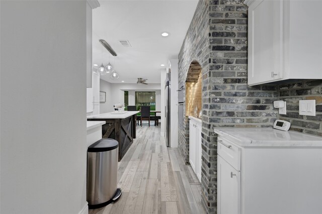 kitchen featuring light stone counters, light hardwood / wood-style floors, hanging light fixtures, and white cabinets