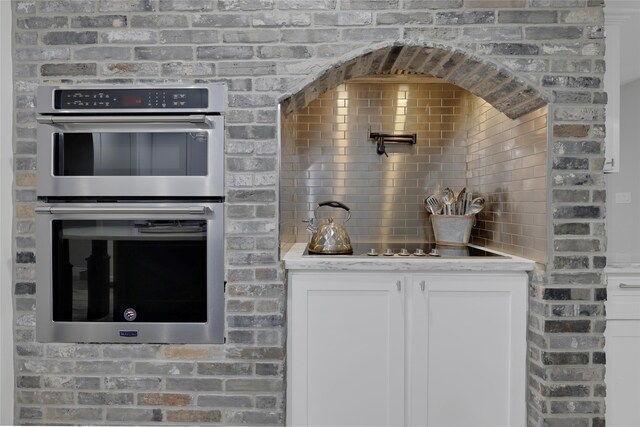 kitchen featuring white cabinetry, brick wall, and stainless steel double oven