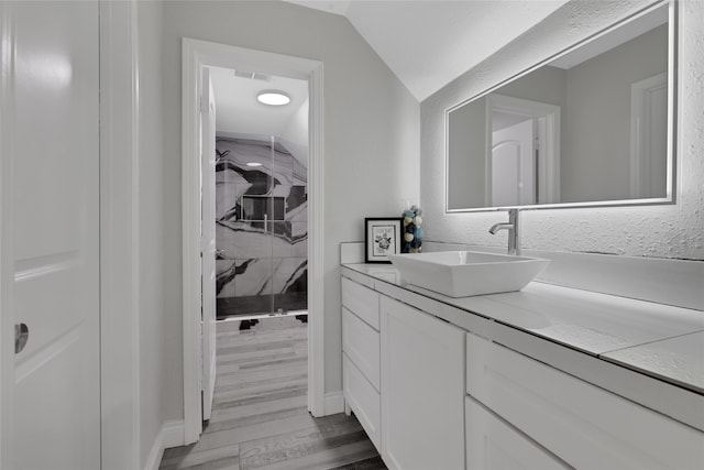 bathroom featuring hardwood / wood-style flooring, vanity, lofted ceiling, and a tile shower