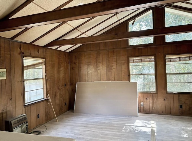 spare room featuring vaulted ceiling with beams, a healthy amount of sunlight, heating unit, and wood walls