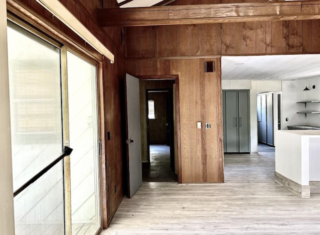 hall featuring light hardwood / wood-style flooring, a wealth of natural light, wooden walls, and beamed ceiling