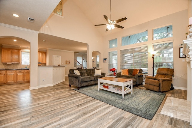 living room featuring ornamental molding, a towering ceiling, a healthy amount of sunlight, and light hardwood / wood-style flooring