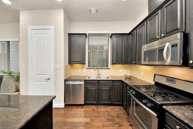 kitchen featuring light wood-type flooring, stainless steel appliances, sink, and dark stone countertops